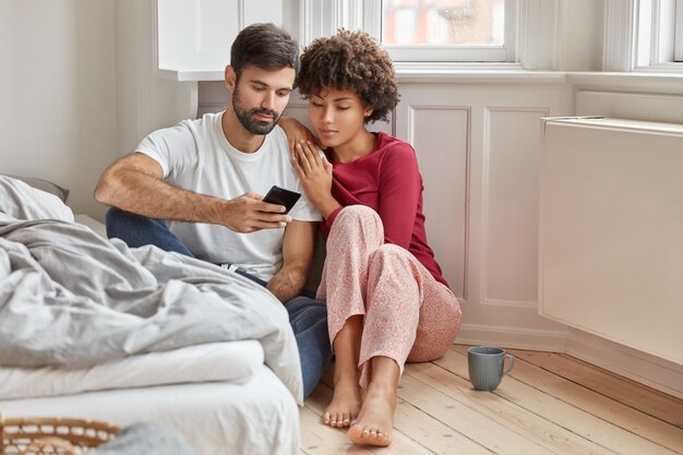 Novio y novia relajado multiétnico sentarse en el piso en casa