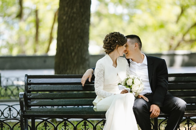 Novio con novia sentarse en un banco y sonreír