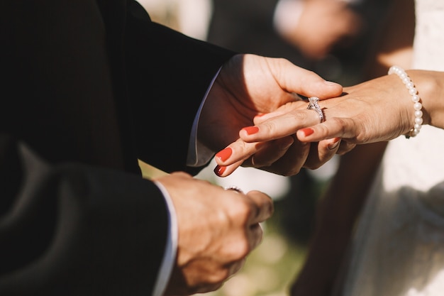 El novio pone un anillo de bodas sobre el dedo de la novia que lo sostiene tierno