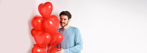 Novio romántico trae globos de corazones rojos en el día de san valentín amante sorpresa en la cita de pie