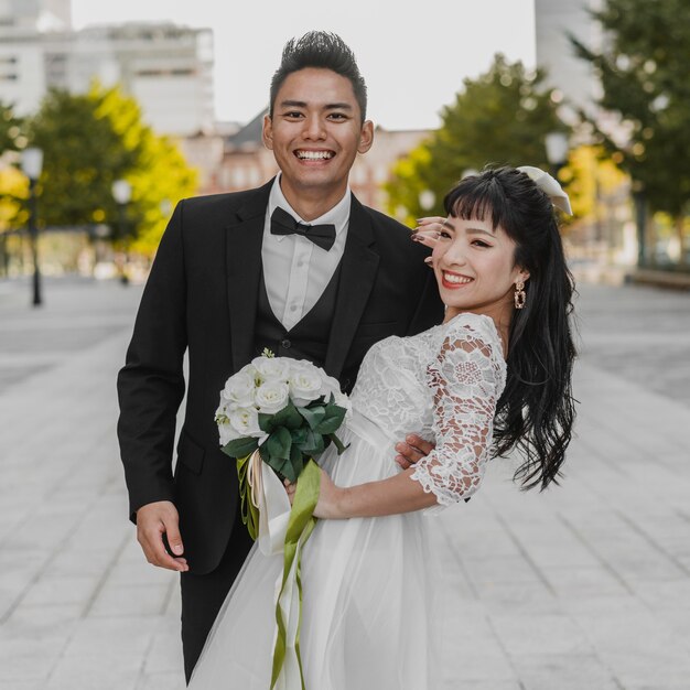 Novio sonriente sosteniendo a su esposa en la calle