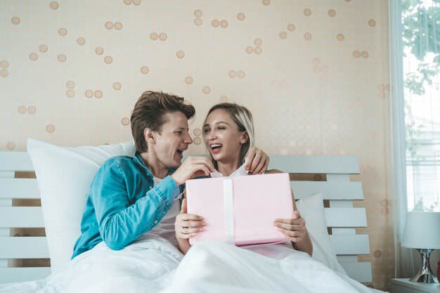 Novio sorprende a su novia con caja de regalo en la cama.