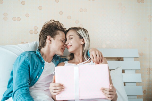 Novio sorprende a su novia con caja de regalo en la cama.