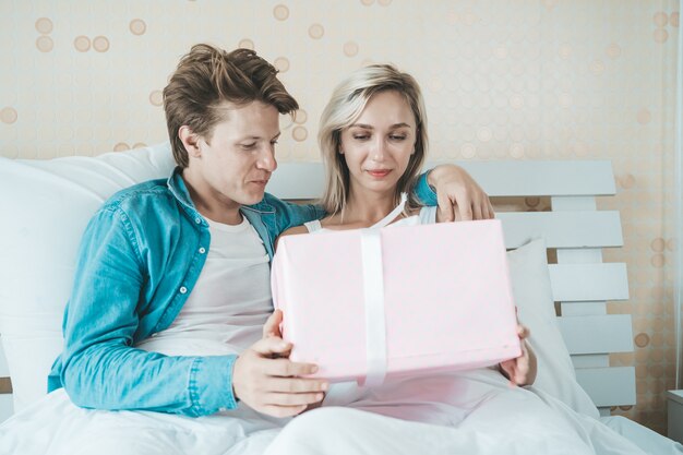 Novio sorprende a su novia con caja de regalo en la cama.