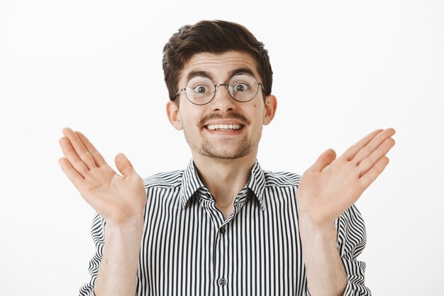 Novio sorprendido nerd con bigote y barba en anteojos, levantando las palmas y sonriendo ampliamente, levantando las cejas por la sorpresa y el asombro, juntando las palmas, complacido y satisfecho con el resultado.