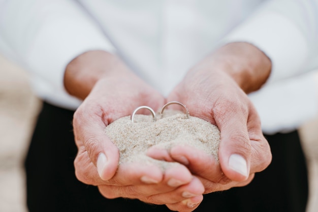 Novio sosteniendo arena y anillos en sus manos