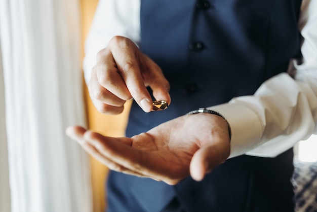 Foto gratuita el novio sostiene el anillo de bodas que está parado delante de la ventana en un hotel r