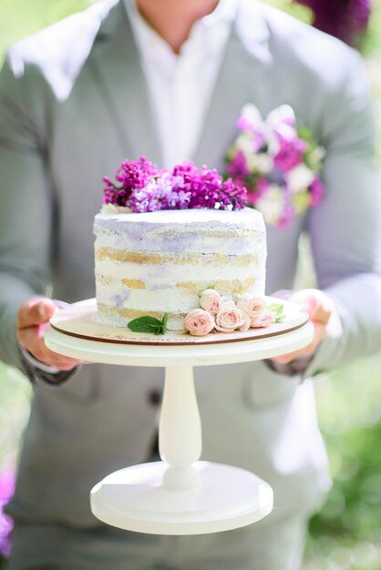 El novio sostiene el pastel de bodas rústico