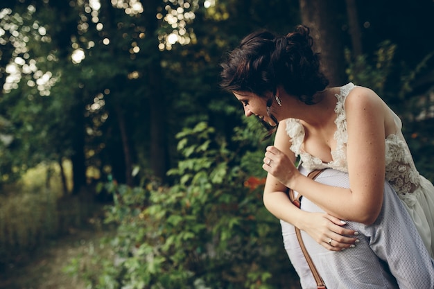 El novio sostiene a su novia en sus brazos en algún lugar de la naturaleza