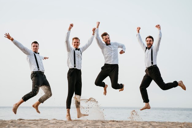 Foto gratuita novio y sus amigos saltando en la playa.