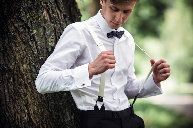 Novio con tirantes apoyándose en un árbol