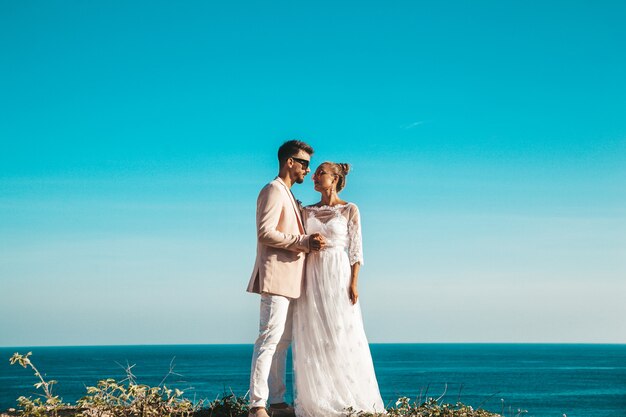 novios posando en el acantilado detrás del cielo azul y el mar