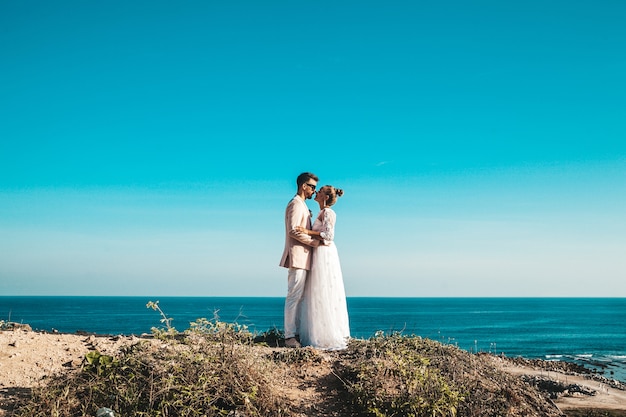 novios posando en el acantilado detrás del cielo azul y el mar