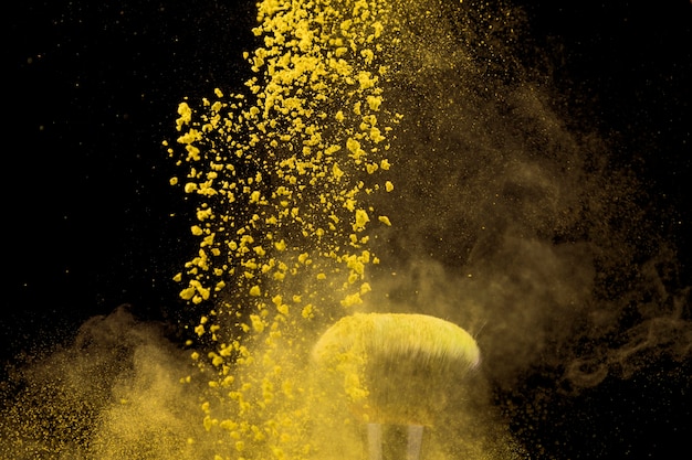 Foto gratuita nube de polvo de maquillaje amarillo y pincel sobre fondo oscuro