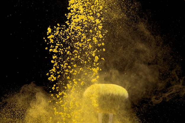 Nube de polvo de maquillaje amarillo y pincel sobre fondo oscuro