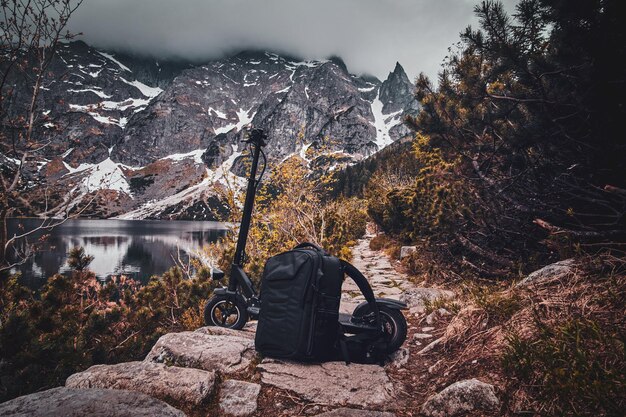 Nubes bajas oscuras, hermosas montañas, lago, pinos y mochila con scooter en el frente.