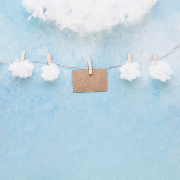 Nubes blancas y tarjeta marrón cuelgan de una cuerda con pinzas para la ropa