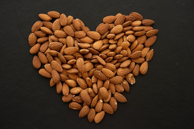 Nueces de almendra formando una forma de corazón sobre fondo negro.