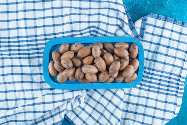 Foto gratuita nueces de pacana en una placa de madera sobre un paño de cocina, sobre la mesa azul.