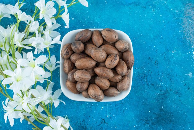 Nueces de pacana en un recipiente junto a flores, sobre la mesa azul.