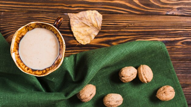 Nueces y servilleta cerca de bebida y hojas de otoño