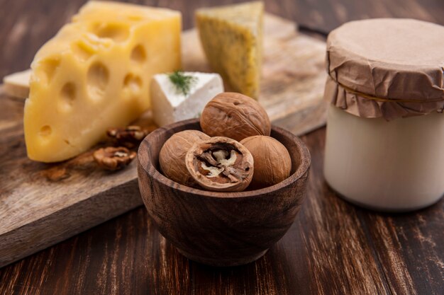 Nueces de vista lateral con variedades de quesos en un soporte con yogur en un frasco sobre un fondo de madera