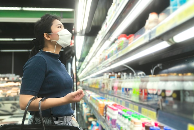 Nueva normalidad después de la epidemia de covid, joven mujer asiática inteligente que compra un nuevo estilo de vida en el supermercado con protector facial o máscara de protección, elija productos de consumo, nuevo estilo de vida normal