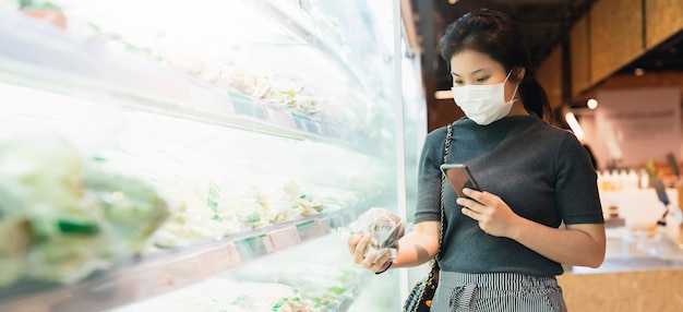 Nueva normalidad después de la epidemia de covid, joven mujer asiática inteligente que compra un nuevo estilo de vida en el supermercado con protector facial o protección con máscara, elija vegetales frescos de frutas, nuevo estilo de vida normal