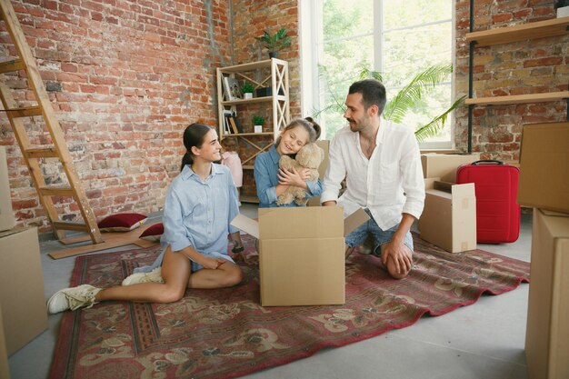 Nueva vida. La familia adulta se mudó a una nueva casa o apartamento. Los cónyuges e hijos se ven felices y confiados. Movimiento, relaciones, concepto de estilo de vida. Desempacando cajas con sus cosas, jugando juntos.