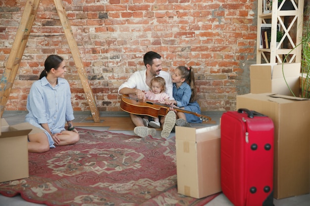 Nueva vida. La familia adulta se mudó a una nueva casa o apartamento. Los cónyuges e hijos se ven felices y confiados. Movimiento, relaciones, concepto de estilo de vida. Desempacando cajas con sus cosas, jugando juntos.