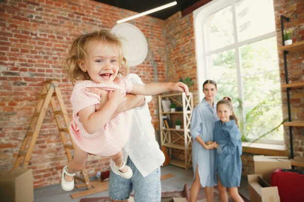 Nueva vida. La familia adulta se mudó a una nueva casa o apartamento. Los cónyuges e hijos se ven felices y confiados. Movimiento, relaciones, concepto de nueva vida. Desempacando cajas con sus cosas, jugando juntos.