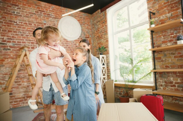 Nueva vida. La familia adulta se mudó a una nueva casa o apartamento. Los cónyuges e hijos se ven felices y confiados. Movimiento, relaciones, concepto de nueva vida. Desempacando cajas con sus cosas, jugando juntos.