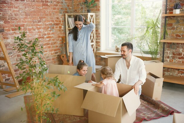 Nueva vida. La familia adulta se mudó a una nueva casa o apartamento. Los cónyuges e hijos se ven felices y confiados. Movimiento, relaciones, concepto de nueva vida. Desempacando cajas con sus cosas, jugando juntos.