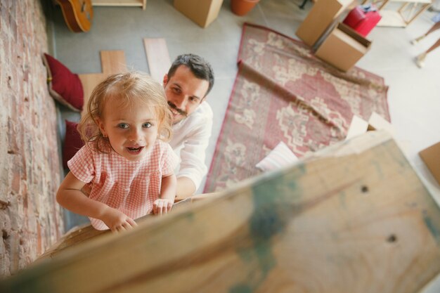 Nueva vida. Padre joven y su hija se mudaron a una nueva casa o apartamento. Luce feliz y confiado. Movimiento, relaciones, concepto de estilo de vida. Jugando juntos, preparándose para la reparación y riendo.