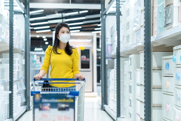 Nuevo estilo de vida normal vestido amarillo femenino asiático que protege las compras de máscaras en los grandes almacenes después del final del período de cuarentena de bloqueo