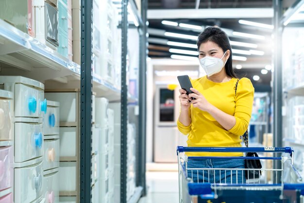 Nuevo estilo de vida normal vestido amarillo femenino asiático que protege las compras de máscaras en los grandes almacenes después del final del período de cuarentena de bloqueo