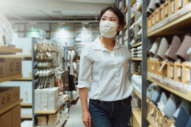 Nuevo estilo de vida normal vestido blanco femenino asiático que protege las compras de máscaras en los grandes almacenes después del final del período de cuarentena de bloqueo