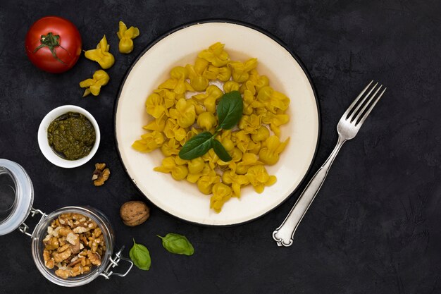 Nuez; tomate; salsa; Pasta de albahaca y tortellini cocida con un tenedor sobre fondo negro