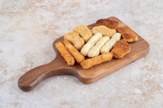 Nuggets crujientes, palitos de queso y salchichas a la parrilla en un plato de madera.