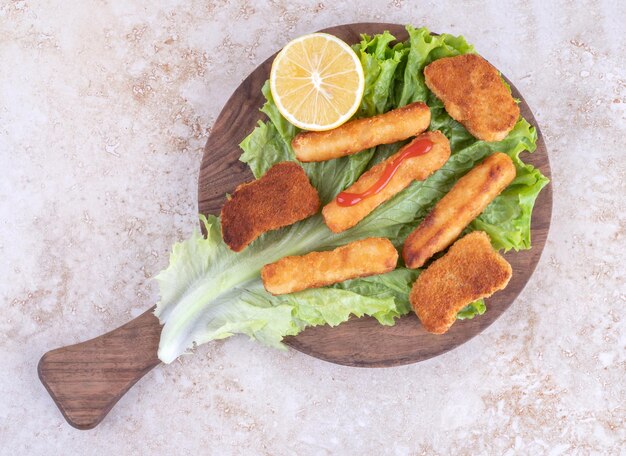 Nuggets de pollo frito y palitos de queso sobre una tabla de madera sobre un trozo de hoja de lechuga.