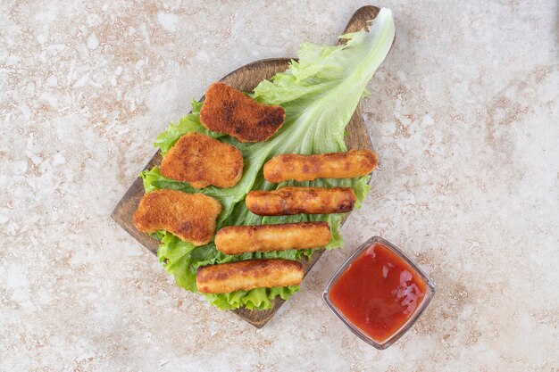 Nuggets de pollo frito y palitos de salchicha a la plancha sobre un trozo de lechuga servidos con salsa de tomate.