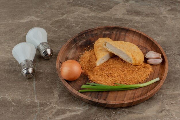 Nuggets de pollo con limón, dos ajos y cebollas sobre tabla de madera con sal y pimienta.