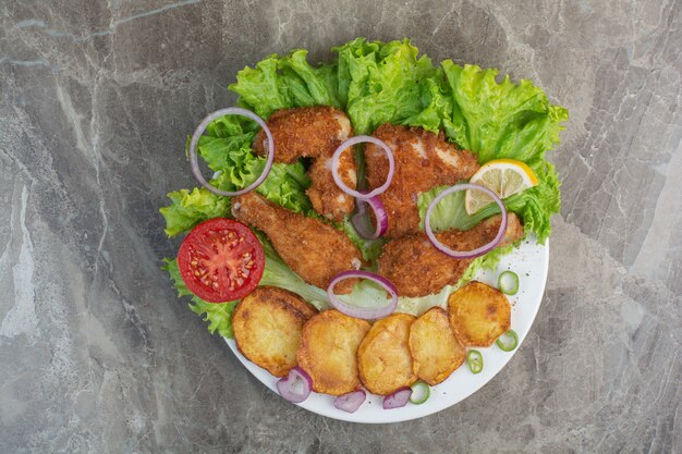 Nuggets de pollo con patatas fritas y cebolla en un plato blanco.