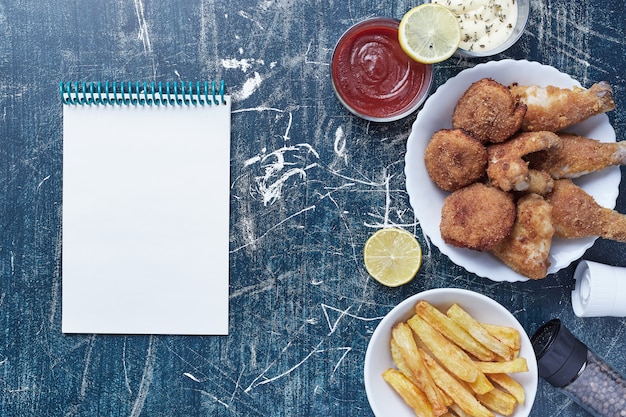 Foto gratuita nuggets de pollo con patatas y salsas con un cuaderno a un lado.