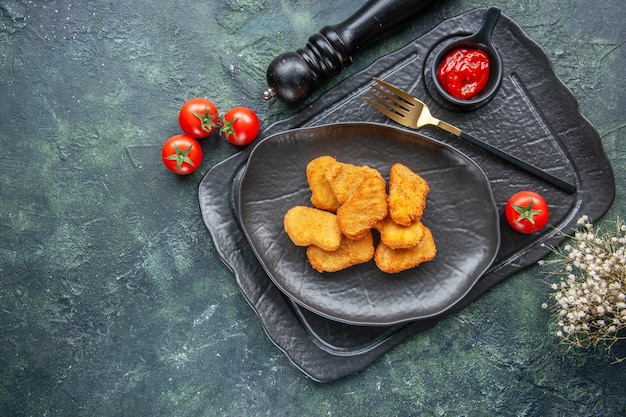 Nuggets de pollo en una placa negra y ketchup de tenedor elegante en bandeja oscura tomates de flor blanca