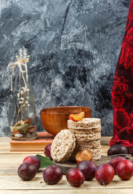 Foto gratuita obleas de arroz de primer plano sobre tabla de cortar redonda con jarrón jarra, un cuenco, ciruelas y pañuelo rojo sobre tabla de madera y superficie de mármol gris oscuro. espacio libre vertical para su texto