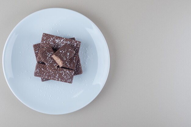 Obleas recubiertas de chocolate apiladas en un plato blanco sobre fondo de mármol.