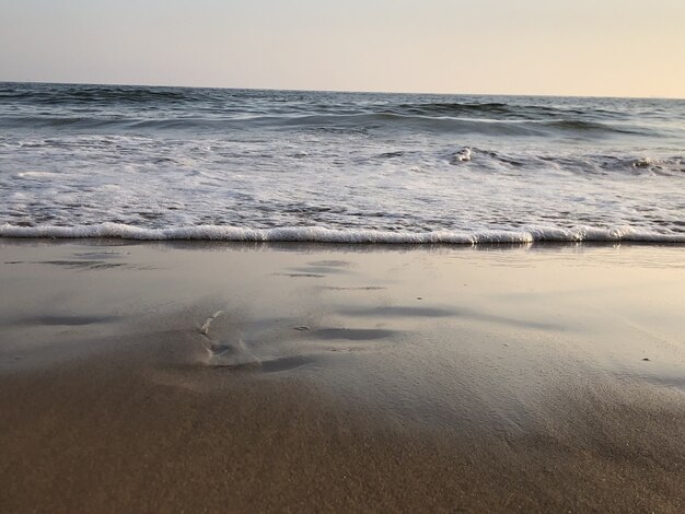 Océano ondulado golpeando la playa de arena y brillando bajo el cielo colorido