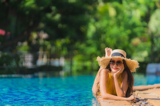 El ocio asiático joven hermoso de la mujer del retrato relaja sonrisa y feliz alrededor de piscina en centro turístico del hotel