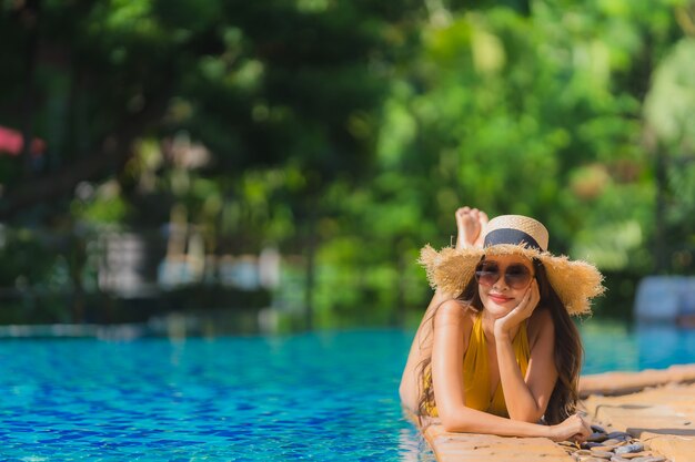 El ocio asiático joven hermoso de la mujer del retrato relaja sonrisa y feliz alrededor de piscina en centro turístico del hotel